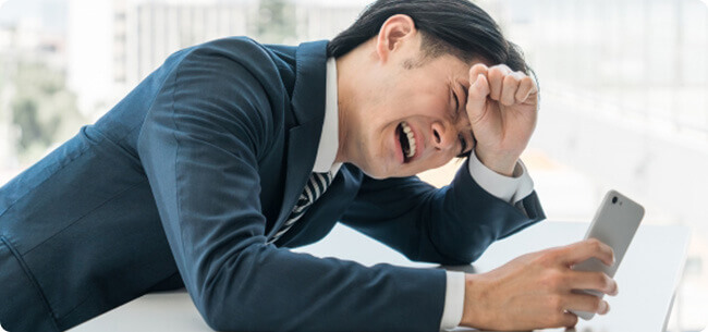 机に肘をつき、頭を抱えて悩むスーツ姿の男性イメージ